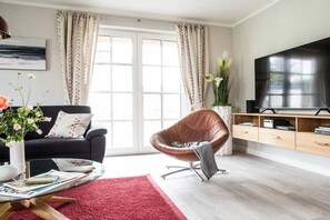 Ein modernes Wohnzimmer mit einer Couch, einem Ledersessel, einem Couchtisch, einem Fernseher und einem Bücherregal.