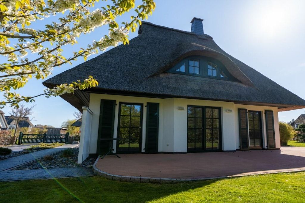 A house with a steeply pitched roof, large windows, and a brick pathway leading to the entrance.