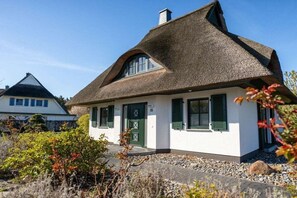 Ein Haus mit einem Strohdach, weißen Wänden und grünen Fensterläden.