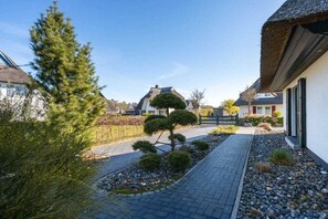 A residential area with a paved pathway, a small tree, and houses with thatched roofs. - Holiday home with 1 bedroom (Fuhlendorf)