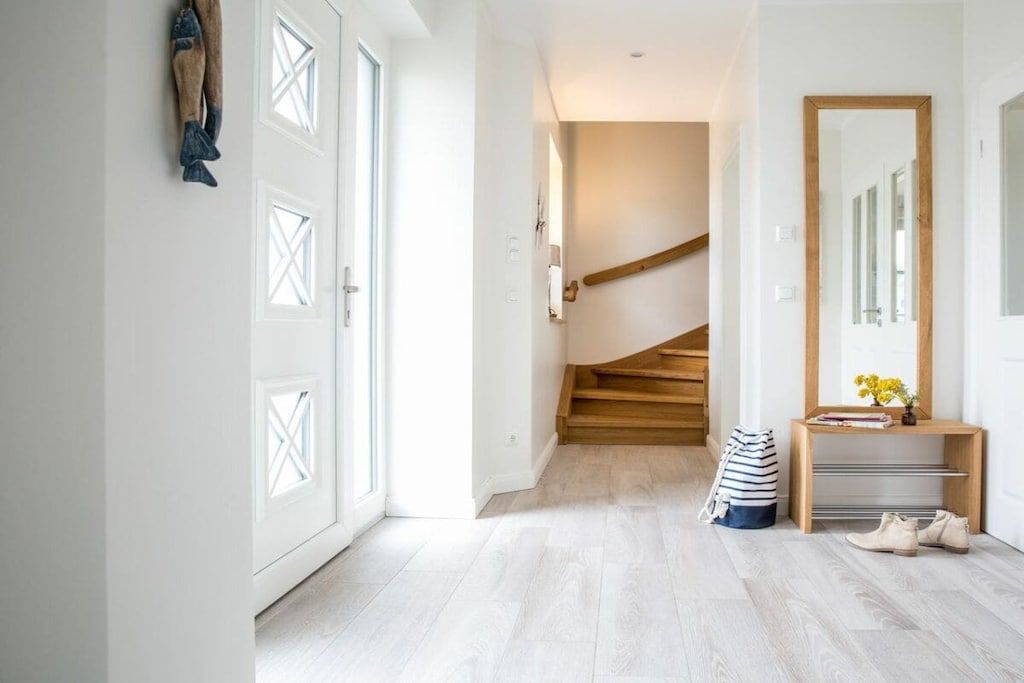 Ein Flur mit einer Holztreppe, einem Spiegel, einer Bank und einem Paar Schuhe.