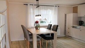 Un comedor con una mesa y sillas de madera, un jarrón con flores y una ventana con cortinas.