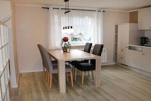 A dining area with a wooden table and chairs, a vase with flowers, and a window with curtains. - Kleist House Apartment 4 (Prerow)