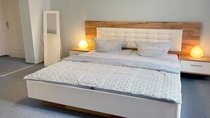 Un dormitorio con una cama, dos mesitas de noche, un tocador, un espejo y una puerta.
