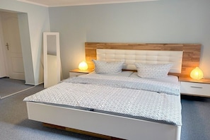 A bedroom with a bed, two bedside tables, a nightstand, a mirror, and a door. - Kleist House Apartment 4 (Prerow)