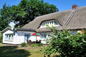 A house with a thatched roof, a white exterior, and a small garden area with a colorful umbrella. - Kleist House Apartment 4 (Prerow)