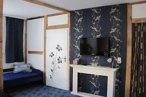 A room with a television mounted on a wall, a fireplace, a blue sofa, and a door with a floral design. - Holiday apartment with 1 bedroom (Sassnitz)