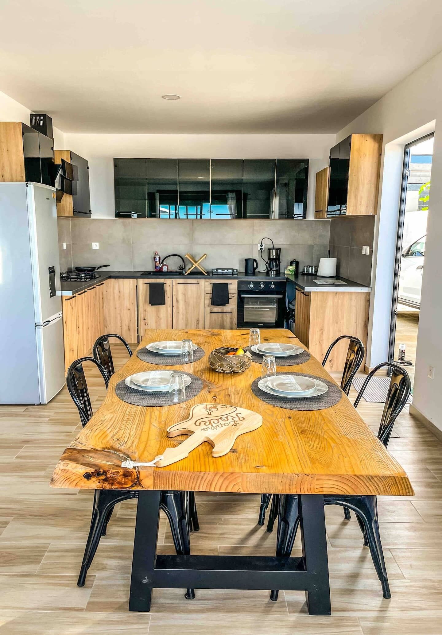 Een moderne keuken met een centraal eiland, houten kasten en een eettafel gedekt voor vier personen.