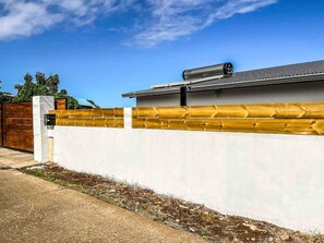 Un edificio moderno con fachada blanca, cerca de madera y portón metálico.