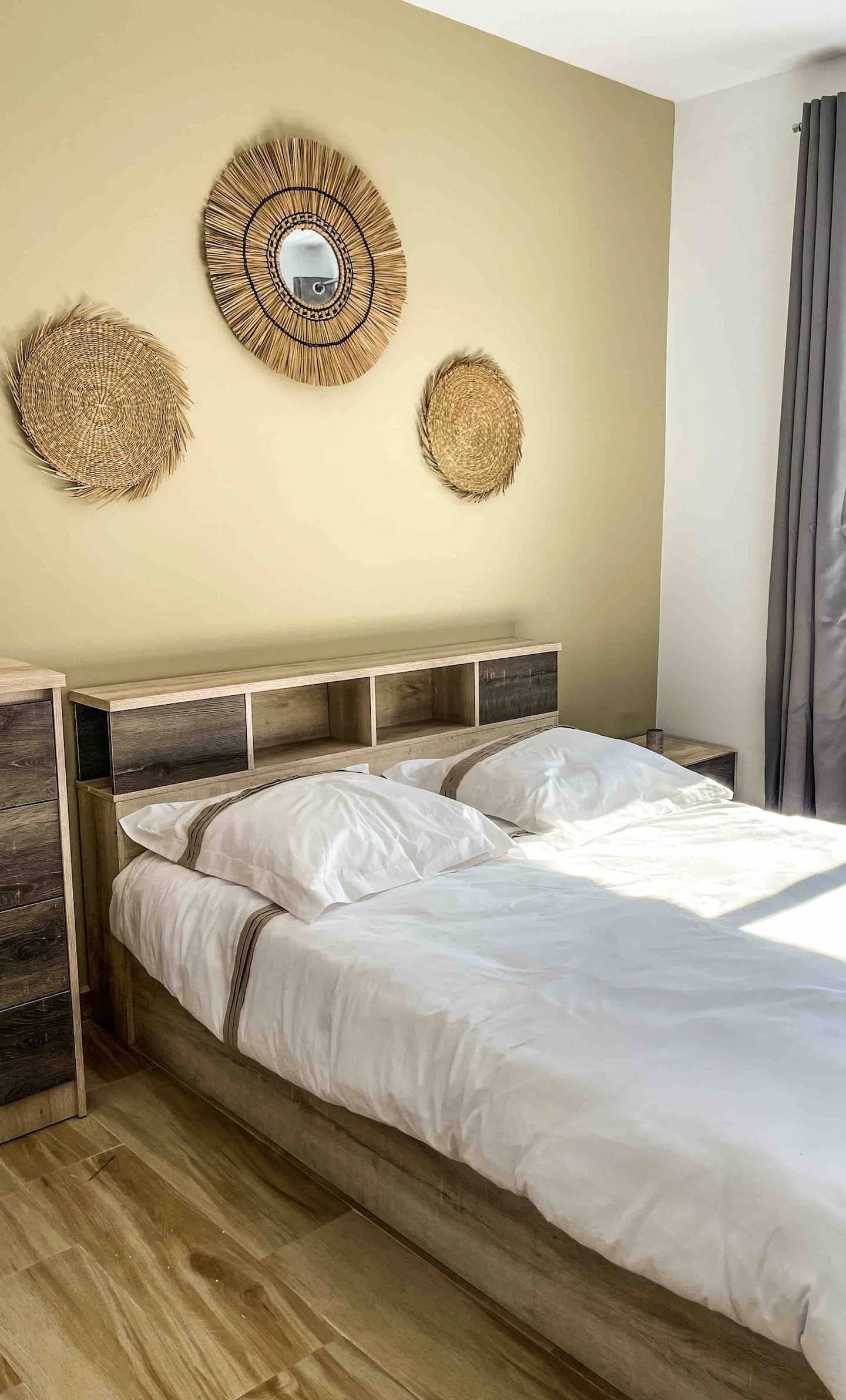 Un dormitorio con cabecera de madera, una cama grande con ropa blanca y tres adornos tejidos en la pared.
