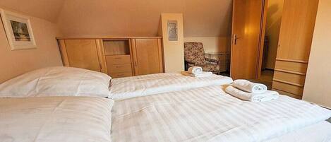 A hotel room with two beds, a wooden wardrobe, a chair, and a small table.