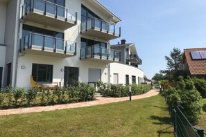 En moderne, fleretagers boligbygning med altaner, en buet facade og en velplejet græsplæne.