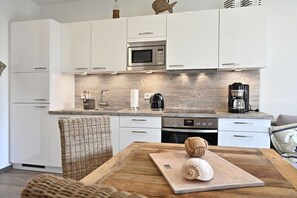 A modern kitchen with white cabinets, a stainless steel microwave, a coffee maker, and a wooden table with a cutting board. - Holiday apartment in Glowe with swimming pool (Glowe)