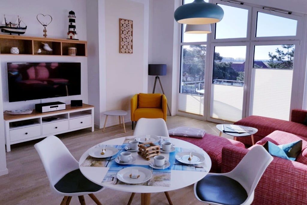 Un salon moderne avec un téléviseur à écran plat, une table à manger pour quatre personnes et un canapé rouge.