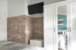 A bedroom with a stone wall, a bed, a wardrobe, and a television mounted on the wall. - Holiday apartment in Glowe with swimming pool (Glowe)