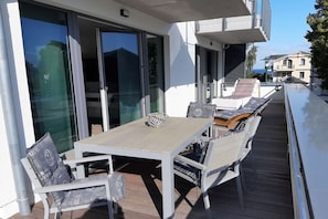 En udendørs terrasse med et bord og stole, en skydedør samt udsigt over de omkringliggende bygninger.