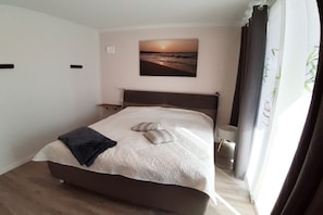 Et soveværelse med en seng, et natbord, en væglampe og et maleri af en solnedgang.