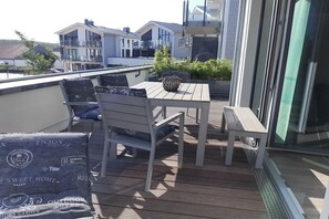 En balkon med et bord, stole, en potteplante og udsigt til omkringliggende bygninger.