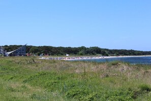 A beach with a modern building in the background, a clear sky, and a grassy foreground. - Holiday apartment in Glowe with swimming pool (Glowe)