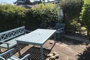An outdoor patio with a table and chairs, surrounded by greenery and a wooden deck.