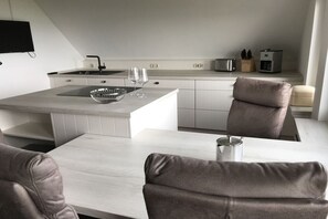 A modern kitchen with a central island, white cabinetry, and a flat-screen TV mounted on the wall.