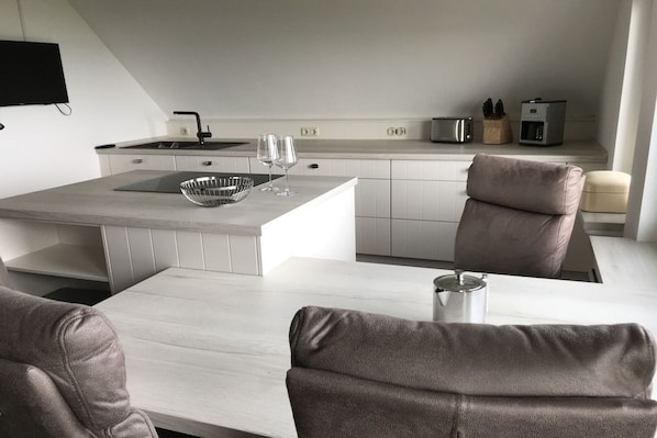 A modern kitchen with a central island, white cabinetry, and a flat-screen TV mounted on the wall.