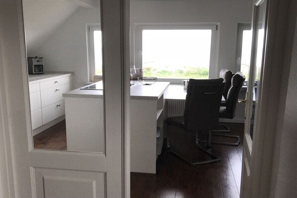 A modern kitchen with white cabinetry, a dining area with a table and chairs, and a view through a glass door.