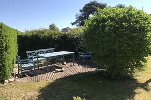 A patio area with a table and chairs, surrounded by a wooden deck and greenery.