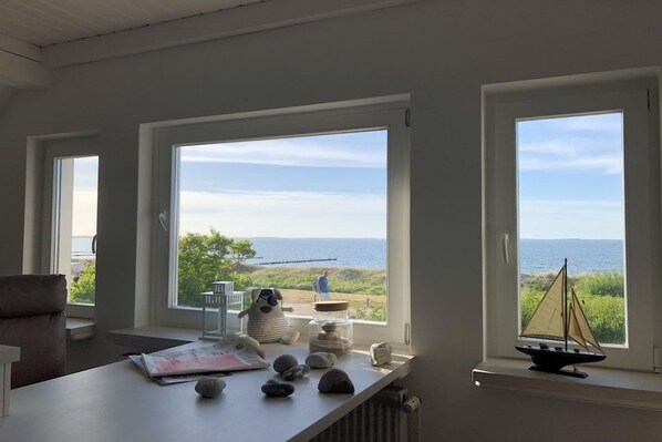 A room with a view of the sea, a table with rocks and a model sailboat, and a chair.