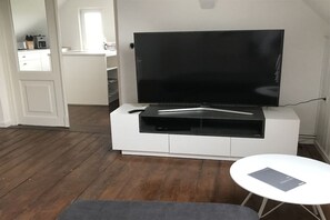 A modern living room with a flat-screen TV on a white entertainment unit, a small round table, and a wooden floor.