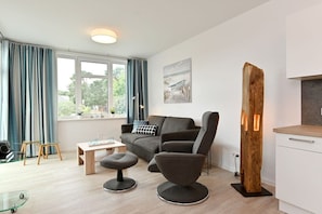 A modern living room with a sofa, a coffee table, and a wooden sculpture. - Holiday apartment in Glowe with swimming pool (Glowe)