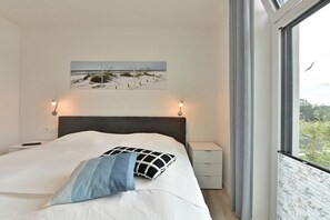 A bedroom with a bed, a nightstand, a wall-mounted picture, and a window with curtains. - Holiday apartment in Glowe with swimming pool (Glowe)