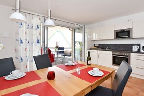 Eine moderne Küche mit weißen Schränken, einer Mikrowelle und einem Backofen. Es gibt einen Esstisch mit Stühlen und einer roten Tischmatte.
