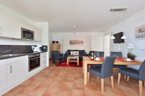 Eine moderne Küche mit weißen Schränken, einem eingebauten Ofen und einem Essbereich mit einem Holztisch und blauen Stühlen.