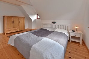 A bedroom with a bed, a nightstand, a wooden wardrobe, and a sloped ceiling. - Holiday home in Wiek with swimming pool (Wiek)