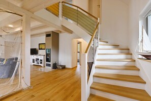 A spacious interior with a wooden staircase, a seating area with a net, and a kitchen area. - Holiday home in Wiek with swimming pool (Wiek)