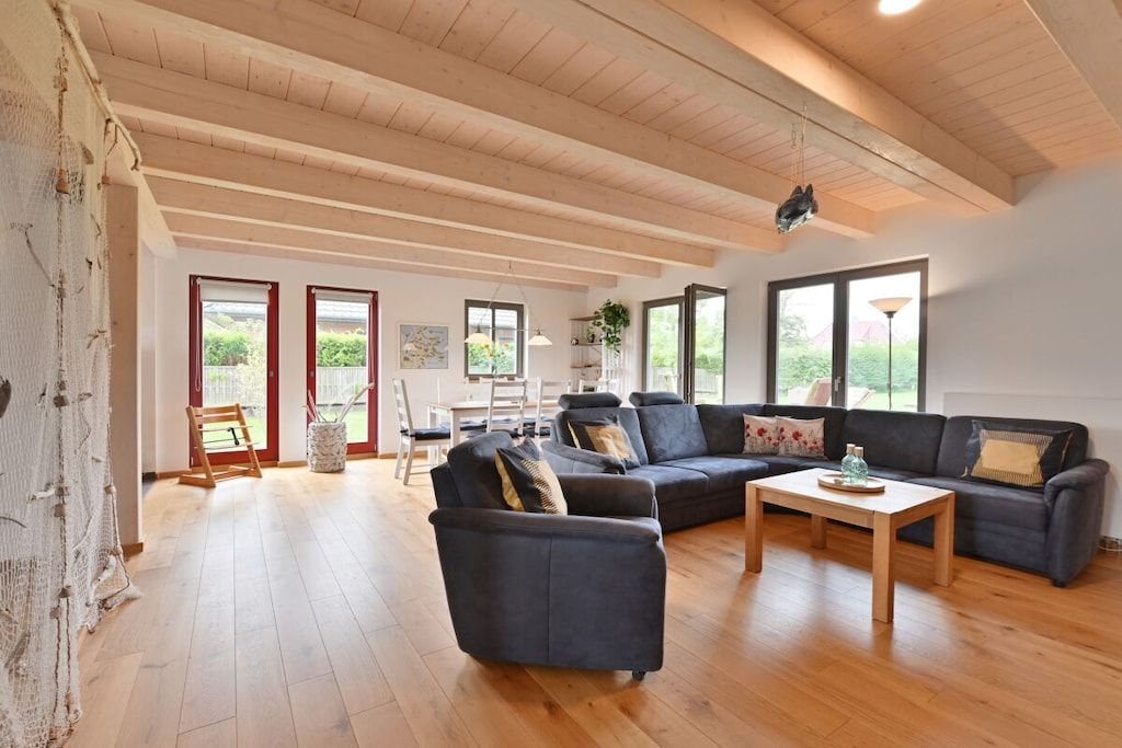 A spacious living room with a high ceiling, wooden beams, and large windows.