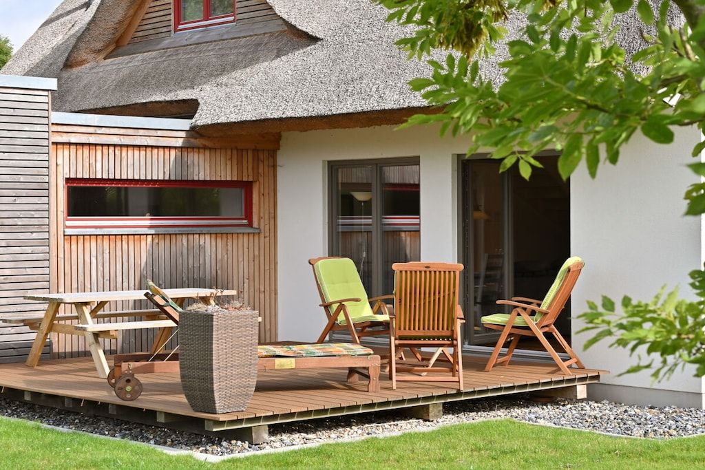 Una casa con techo de paja, terraza de madera y mobiliario exterior.