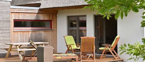 Una casa con techo de paja, terraza de madera y mobiliario exterior.