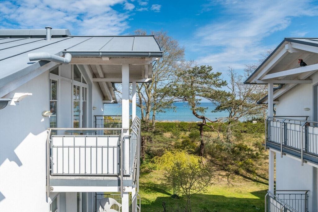 A modern building with a balcony overlooking a grassy area and a body of water.