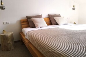 Quarto com estrutura de cama de madeira, colchão branco e manta listrada. Há duas mesas de cabeceira com luminárias.