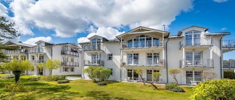 Un immeuble résidentiel à plusieurs étages, doté de balcons, d’une pelouse bien entretenue et surplombant un ciel bleu dégagé.