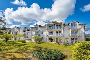 A multi-story residential building with balconies, a well-maintained lawn, and a clear blue sky. - Holiday apartment with 2 bedrooms (Juliusruh)
