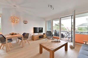 Ein modernes Wohnzimmer mit Couchtisch aus Holz, einem Fernseher und einem Essbereich mit Stühlen.
