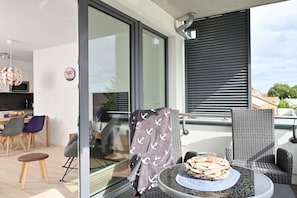 En moderne balkon med glasdør, et spiseområde med stole og bord, og udsigt til himlen.
