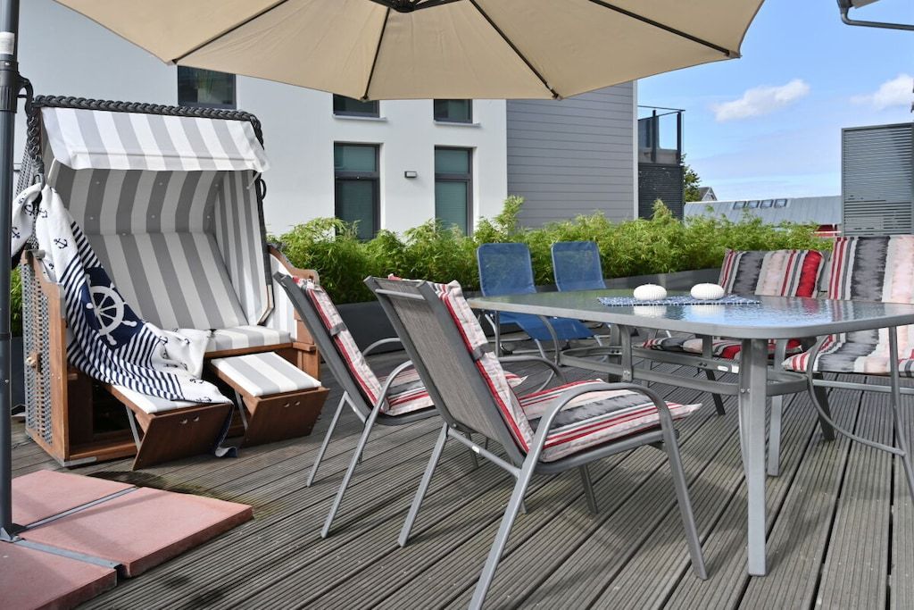 Un espace extérieur aménagé avec des fauteuils de jardin à rayures, une table ronde et un grand parasol.