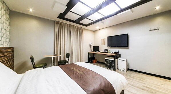 A hotel room with a bed, a desk with a computer, a TV, and a window with curtains. - KOZAZA (Changwon)