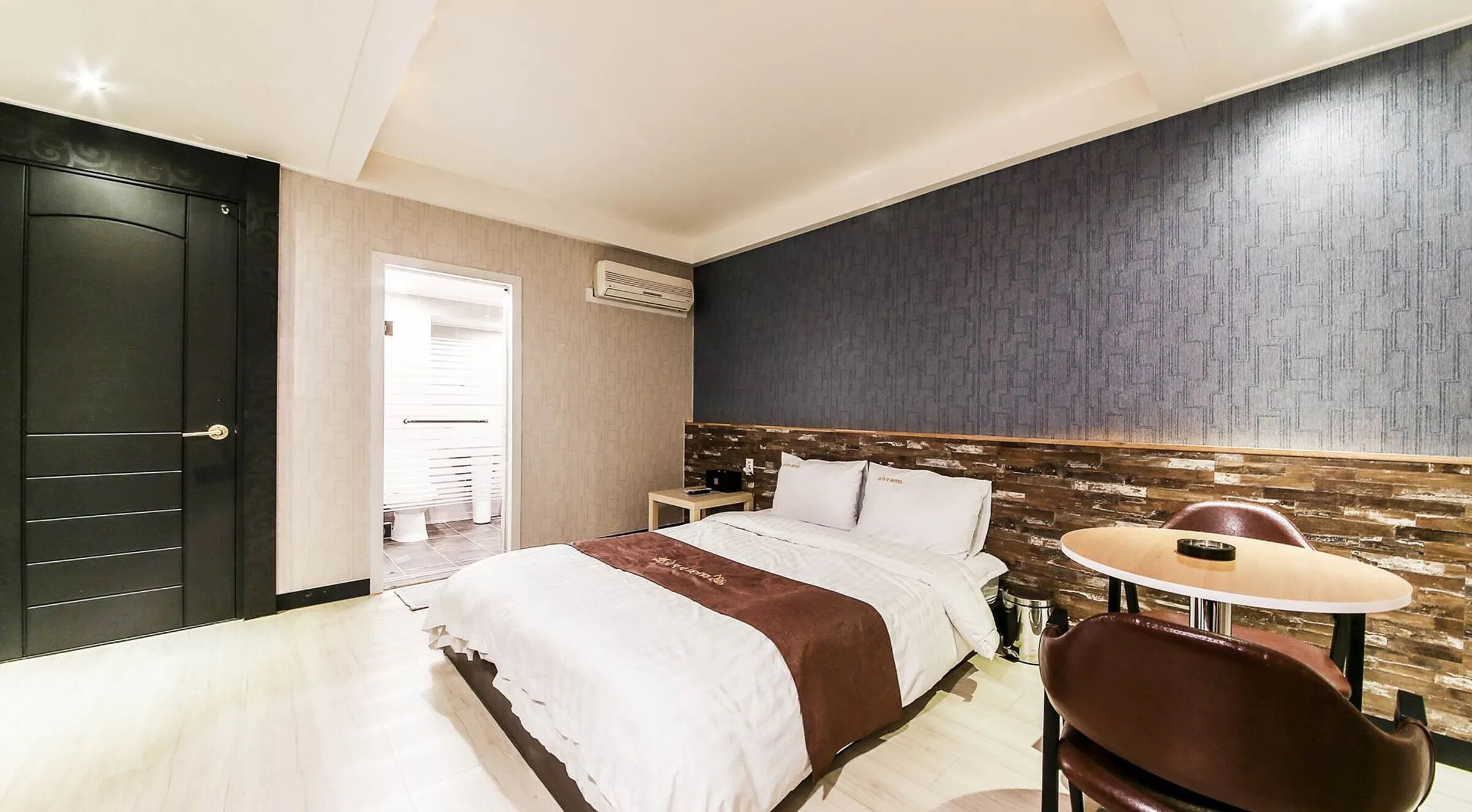 A hotel room with a bed, a bedside table, a chair, and a small round table.