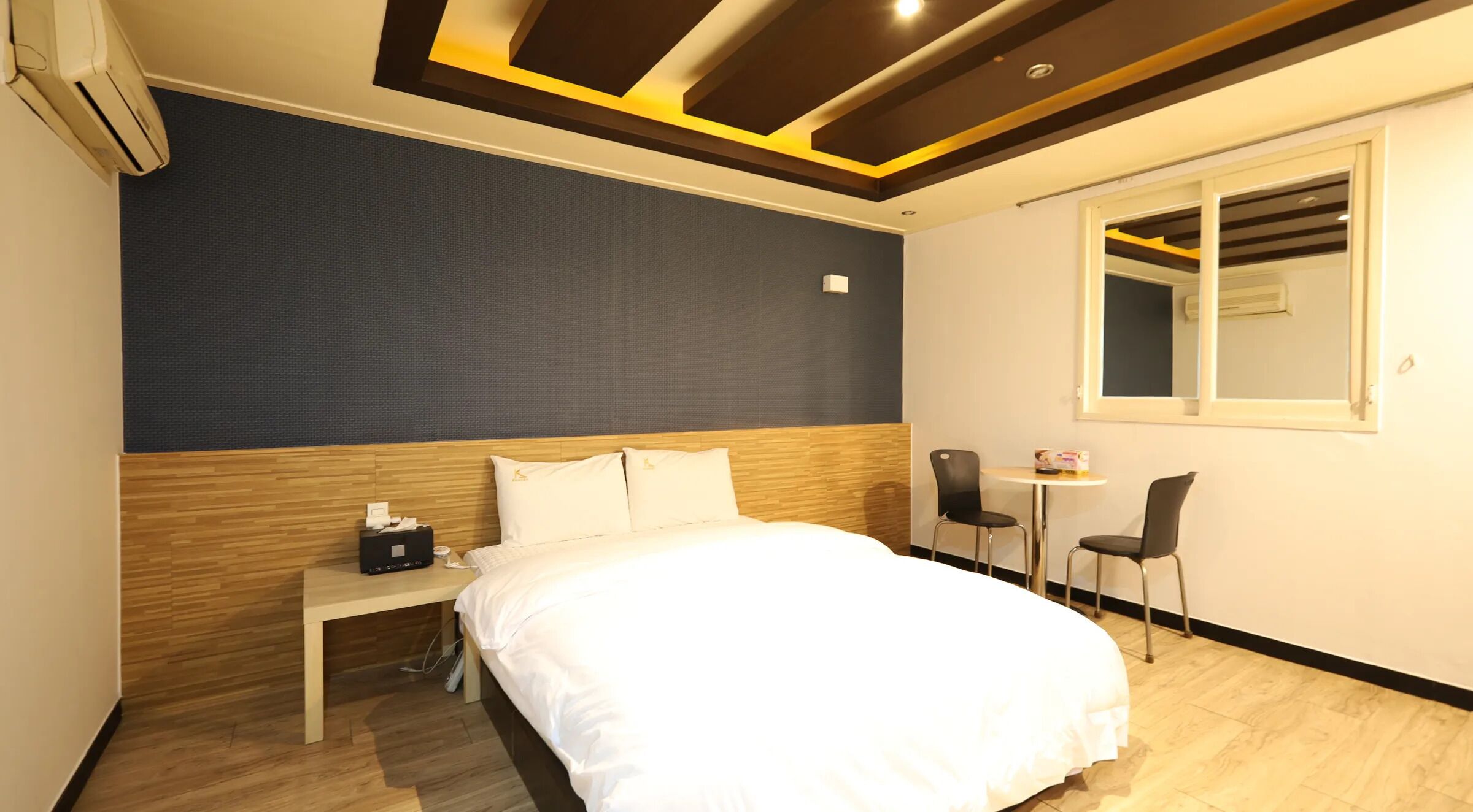 Una habitación de hotel con una cama, mesita de noche y un pequeño escritorio con una silla.