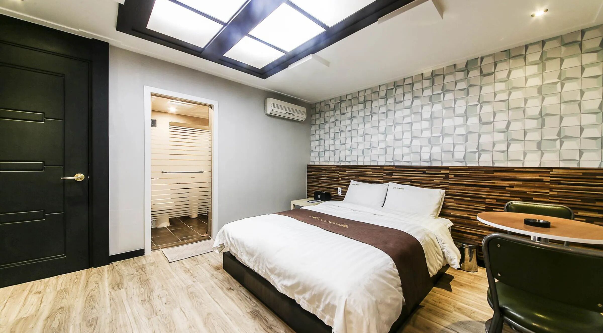 Een hotelkamer met dakraam, een bed met houten hoofdbord, een nachtkastje en een groene stoel.